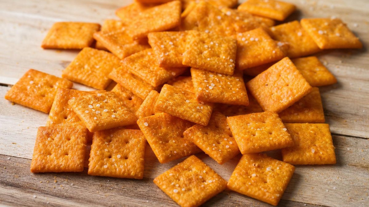 A pile of small square baked cheese crackers on a rustic wooden board