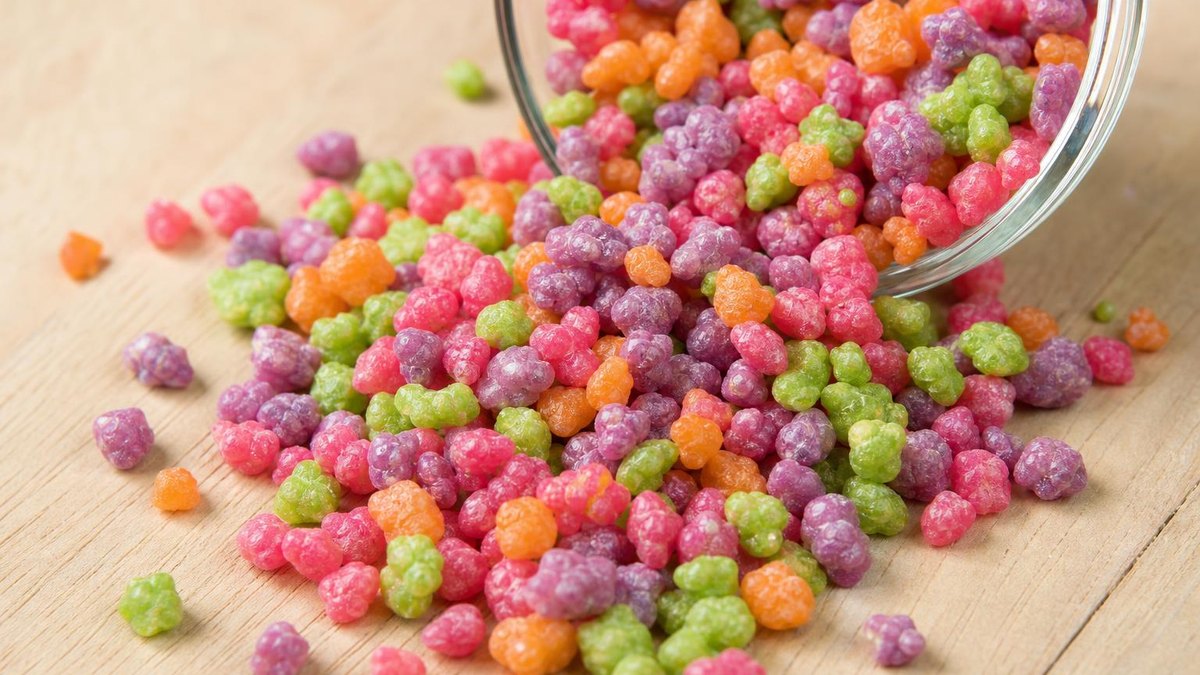 Tiny multicoloured crunchy candy pellets spilling from a small glass dish