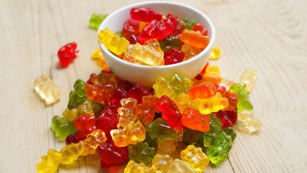 Assorted colourful gummy bears spilling from a small white bowl