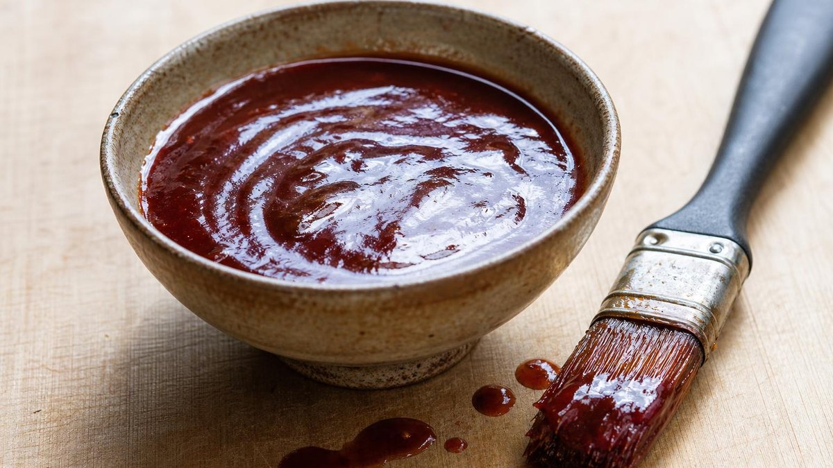A rustic bowl of thick glossy barbecue sauce with a basting brush